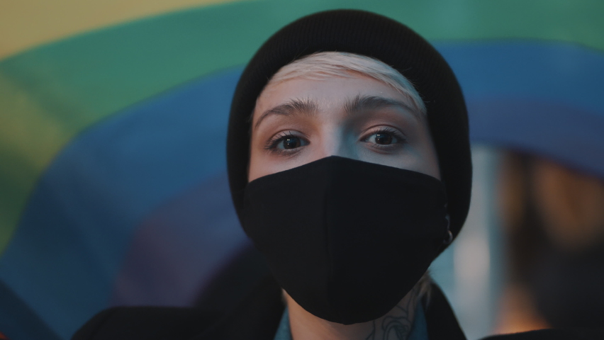 Portrait of young woman with face mask and rainbow flag. Concept of sexual orientation acceptance, protest during coronavirus outbreak. High quality 4k footage