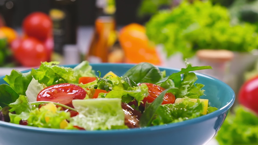 Fresh salad with lettuce leaves and tomato falling into bowl, served with healthy food ingredients on white table, slow motion