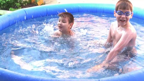 Two boys bathe and frolic in the pool in the summer, splashing water.