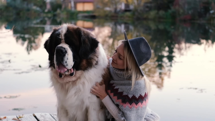 Attractive girl with her friend big dog sit near the lake in nature
