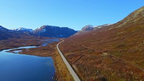 Mountain pass road cutting through rugged terrain and lakes in the highlands in autumn. Aerial video.