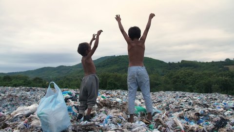 Poverty Boys Standing On Garbage Dump With Arms Raised
