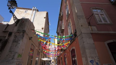 LISBON - JULY 14, 2019: Wired tinsel and buntings hang between buildings, lane decoration at old city, famous Upper district of Lisbon. Walk around Bairro Alto at sunny day. Old houses at narrow lane