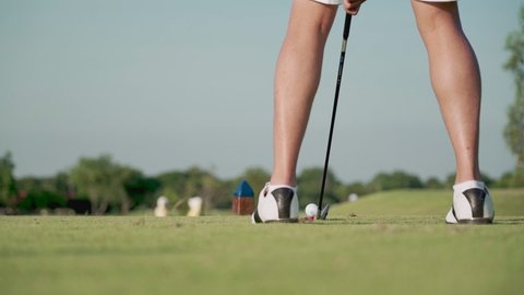 low angle shot lower body of Young adult male golfer driving tee off golf on green grass professional golf course. rear view golfer swinging and hitting golf ball on beautiful grass, slow motion
