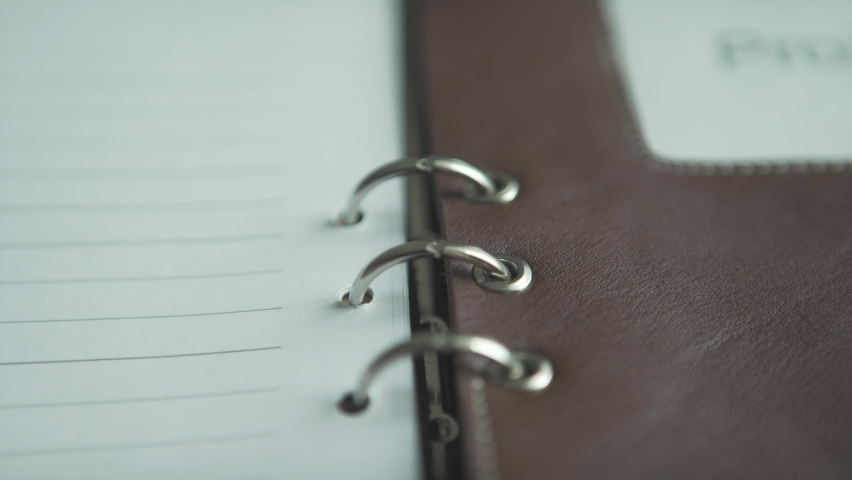 Close up shot of opening metal steel binding of brown leather case note pad daily planner bullet journal on wooden table