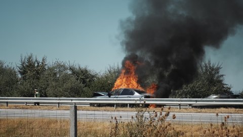 Car burns with big flame and black smoke on a major highway after a summer accident on a sunny day blu sky. Road accident. Traffic incident. Danger. Fire