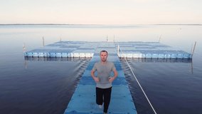 Aerial footage of guy running in on a summer day at sunset on the pier with the sea. Training near water. Struggle with bad habits. Sport and recreation. Preparation for competitions. Outdoors