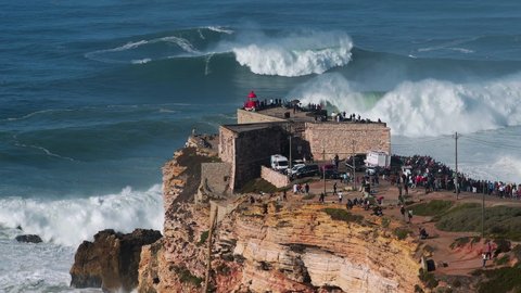 Surfers riding huge waves near the Fort of Sao Miguel Arcanjo Lighthouse in Nazare, Portugal. Nazare is famously known to surfers for having the largest waves in the world.