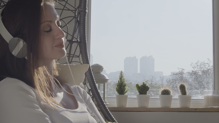 Girl at home sitting on modern chair in front of window, listening music and nap