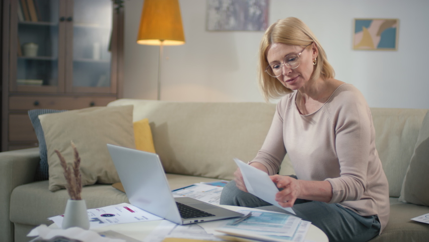 Medium footage of middle aged caucasian woman checking bills and payments at home going through papers getting frustrated about financial loss and crisis
