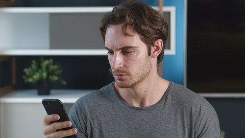 Man is shocked terrible message on his smartphone at home apartment background. Unpleasantly surprised young male reacting message on his mobile phone.