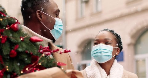 Close up portrait of happy African American family in masks standing on street in winter city with little new year tree. Joyful young couple in good mood outdoors, Christmas concept. Winter season