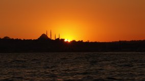 City silhouette with stunning orange sunset and dark shapes of landmarks, mosques, buildings and ocean. 4k sliding cityscape video shot at golden hour.