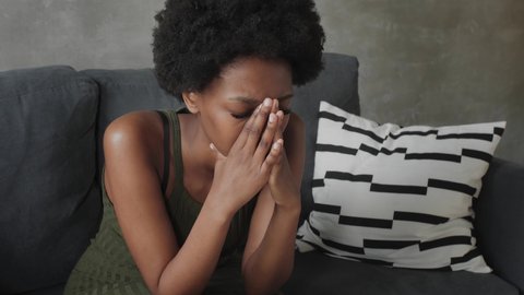 Afro american woman with thoughtful face sitting on couch