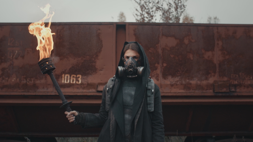 Woman in cyberpunk suit and gas mask standing by rusty train carriage hold burning torch in hand and looking into camera. Dystopian warrior concept, female survivor in abandoned city. Post apocalypse Royalty-Free Stock Footage #1061799514