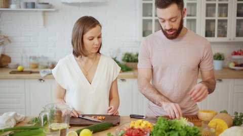 Young couple cooking together and talking in kitchen preparing dinner at home 