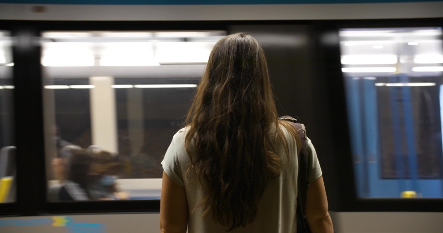 Rear view of young woman with backpack, wearing covid-19 face mask for protection while waiting at platform of metro station looking at passing train Royalty-Free Stock Footage #1061800852