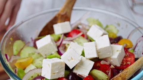 Adding feta cheese cubes into a Greek Salad on the table in 4K. Concept of preparing Vegetable Salad step by step.