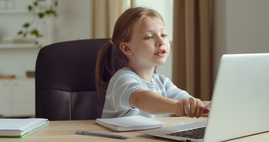 Portrait of cute studious young girl caucasian child using laptop computer speaking with teacher online and writing on notebook, learning and doing homework sitting at home table, coronavirus epidemic | Shutterstock HD Video #1061804236
