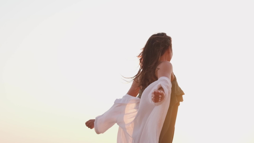 beautiful girl dancing on the beach in a white shirt. Free girl with long hair in a white shirt dances in the sunset. Healthy woman dancing on the beach.