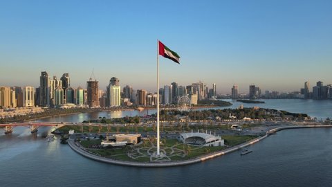 Aerial view of the Flag of the United Arab Emirates waving in the air, the Blue sky in Background, The national symbol of UAE over Sharjah's Flag Island, United Arab Emirates, 4K Video