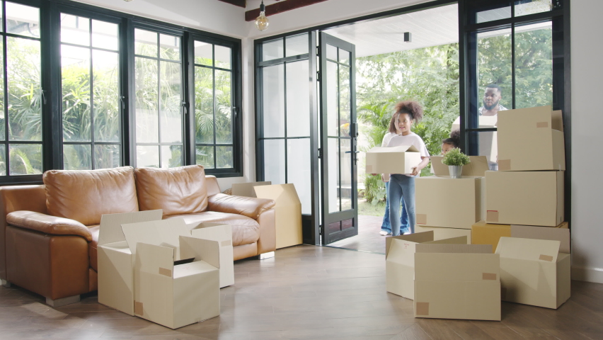 Happy African American young family bought new house. Mom, Dad, and child smiling happy hold cardboard boxes for move object walking into big modern home. New real estate dwelling, loan and mortgage. Royalty-Free Stock Footage #1061809933