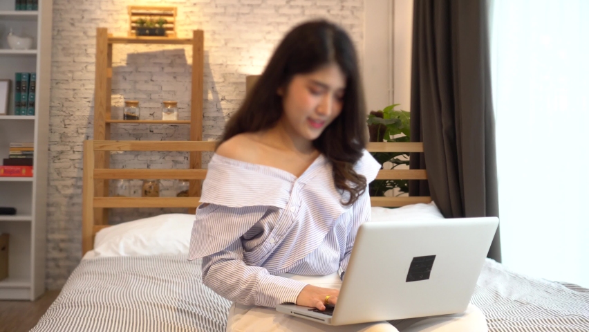 Portrait of happy 20s aged Asian woman in casual clothing using a computer laptop in living room at home. Work from home and remote working concept. | Shutterstock HD Video #1061810221