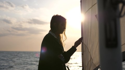 Young woman sailing yacht and using a smartphone shows a view during sunset