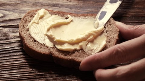 Close-up butter spreading on rustic rye bread with metal knife on wooden table