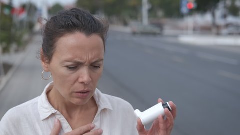 Breath an inhaler in the street. A woman use an inhaler by the road with car. A concept of asthma attack because of pollution.