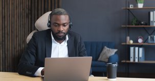 Portrait of Confident Man, Businessman is smiling at the Camera, sitting at Home Office. Young African American is wearing a Headset, holding a Seminar, Conference, Webinar. Online Job. Quarantine.