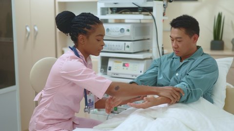 African american female medical specialist doing doctor checkup examining asian male patient checking pulse, heartrate and pressure. Hospital. Doctor appointment. Multirace people.