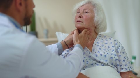 Caucasian doctor therapist checking thyroid throat touching neck of elderly female patient in the hospital room. Healthcare specialist. Medicare. Treatment. Doctor checkup.