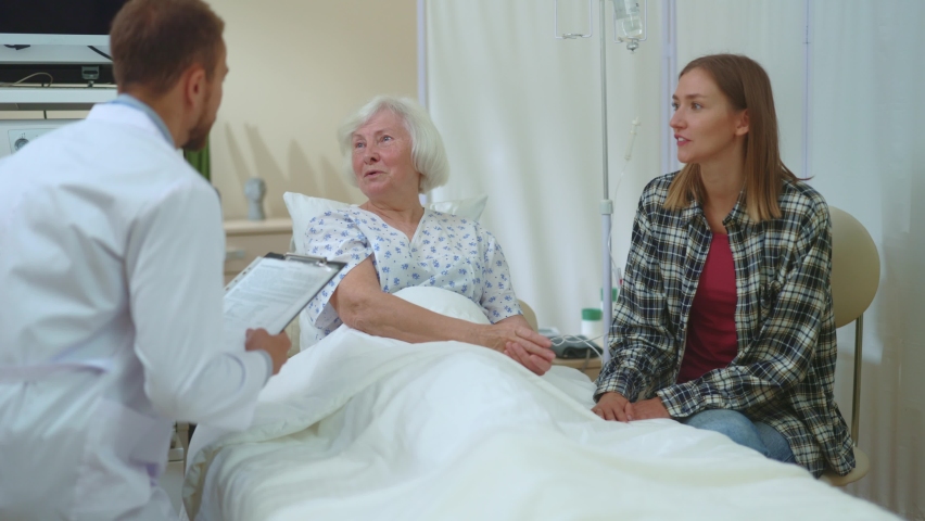 Caucasian fajmily grandma and young woman talking in hospital room when doctor comes. Young healthcare specialist physician consulting two women. Doctor appointment. Hospital. | Shutterstock HD Video #1061819338