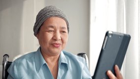 Happy Asian elderly patient sitting on wheelchair and making video call with tablet at hospital. elderly people healthcare concept.