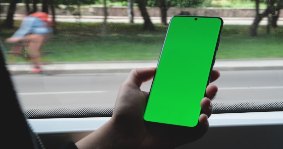 Woman`s Hand is holding Cell Phone near the Window on the Road in Bus, Tram. Cars are driving on the Backgroud behind the Window, good Weather outside. Vertical Position, watching Seminar, Webinar. Royalty-Free Stock Footage #1061820316
