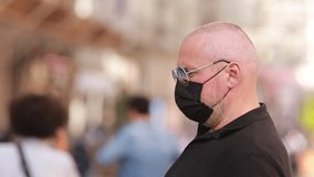 Video, emotional adult man in a protective mask and sunglasses on a city street on a summer day, defocus background.