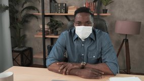 Confident young african businessman in face mask office workplace. Mixed race entrepreneur talking doing online video chat job interview sit at desk, webcamera view. Distance work webcam. Coronavirus
