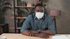 Confident young african businessman in face mask office workplace. Mixed race entrepreneur talking doing online video chat job interview sit at desk, webcamera view. Distance work webcam. Coronavirus - Powered by Shutterstock - Get 15% off with code: PIKWIZARD15
