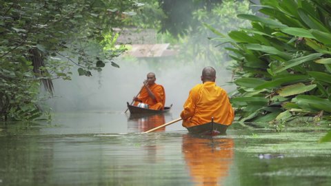 Local Thai monks with alms. Men sailing wooden boat in canal or river for receiving food, Traditional Thai Buddhism lifestyle. Asia, Thailand. 