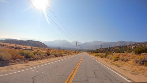 Driving towards the mountains along a desert road with the sun high in the sky - point of view