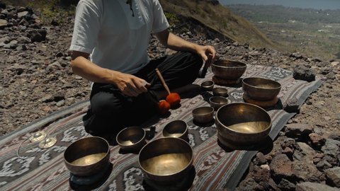 A young Asian guy playing Tibetan singing copper cups on a viewing mountain in nature