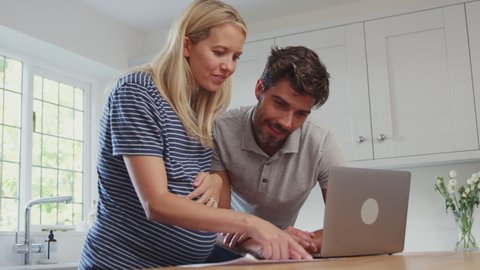 Couple with pregnant wife at home buying products or services online using laptop - shot in slow motion