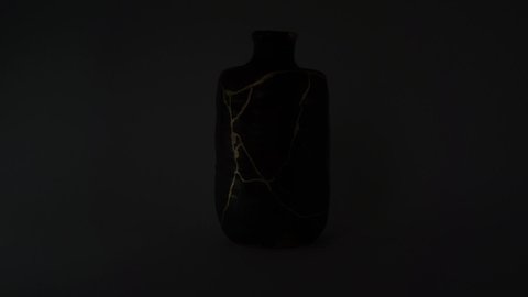 Kintsugi bottle with real gold cracks. Gold cracks lighted up.
Dark brown pottery. Trauma representation. Kintsugi, the Japanese art of restoring pottery with gold.