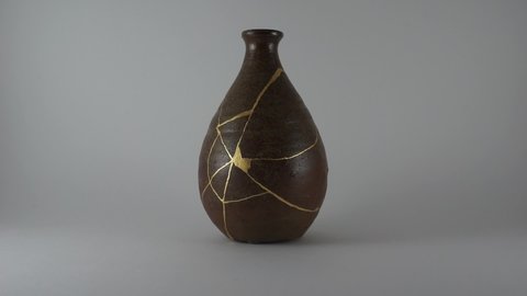 Kintsugi bottle with real gold cracks. Gold cracks lighted up.
Dark brown pottery. Trauma representation. Kintsugi, the Japanese art of restoring pottery with gold.