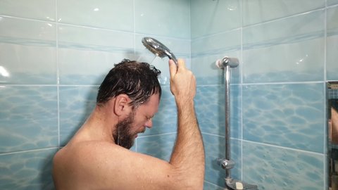 bearded man in the shower washes under cold water and freezes