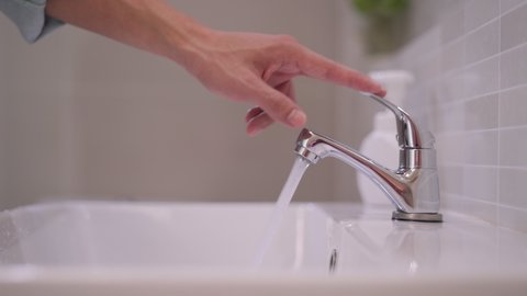 The faucet in the bathroom with running water. Man keeps turning off the water to save water energy and protect the environment.