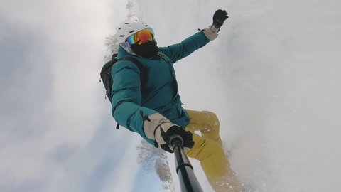 Person on snowboard with selfie stick falling in deep snowdrift. Camera dive in beatiful wave of pure white snow. Beautiful background of mountain range. Concept of extreme sport, vacation, freeride.