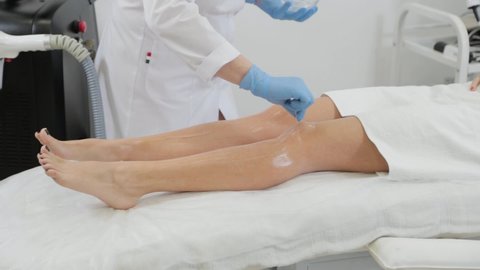 Woman beautician applies laser depilation gel to client.