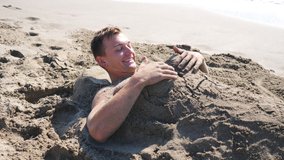 Young man waking up on beach with funny sand figure of woman at himself. Guy showing emotions of surprise and joy touching sand sculpture on him. Man resting on resort lying on seashore. Close up - Powered by Shutterstock - Get 15% off with code: PIKWIZARD15